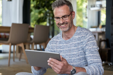 Smiling mature man at home using a tablet - DIGF04394