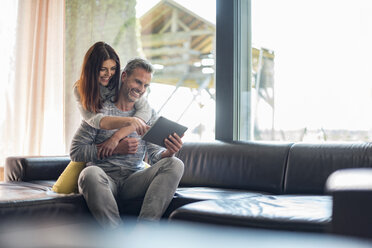 Happy couple on couch at home sharing a tablet - DIGF04399