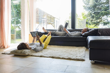 Couple relaxing in living room at home using tablet and laptop - DIGF04400