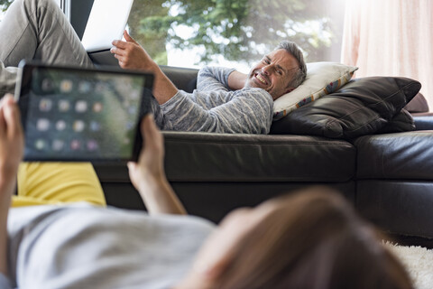 Ehepaar entspannt sich im Wohnzimmer zu Hause mit Tablet und Laptop, lizenzfreies Stockfoto