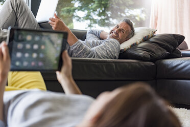 Couple relaxing in living room at home using tablet and laptop - DIGF04401