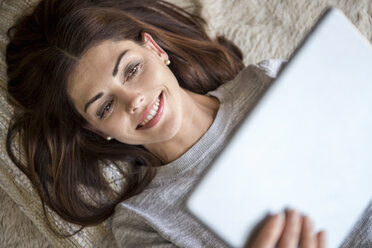 Smiling woman lying on carpet using a tablet - DIGF04402