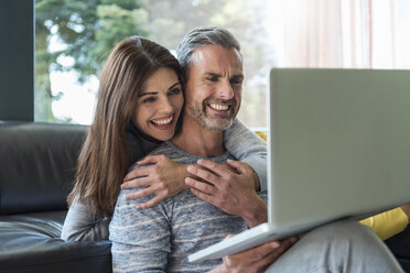 Happy couple on couch at home sharing a laptop - DIGF04403