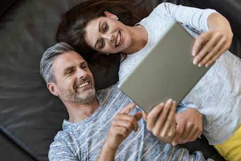 Glückliches Paar, das zu Hause auf der Couch liegt und sich ein Tablet teilt - DIGF04405