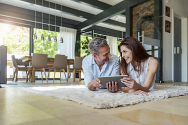 Happy couple lying on carpet at home sharing a tablet - DIGF04415