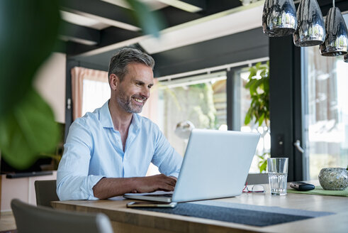 Smiling mature man at home using a laptop at table - DIGF04419