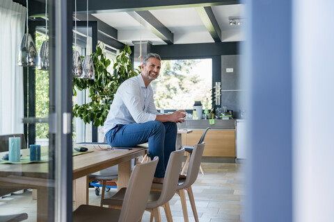 Smiling mature man at home sitting on table with cup of coffee stock photo