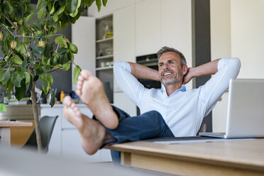 Smiling mature man relaxing at home with laptop on table - DIGF04424