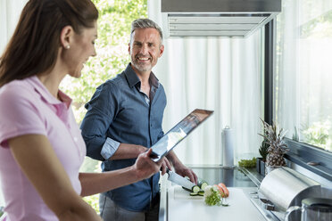 Happy couple in kitchen at home cooking and using a tablet - DIGF04445