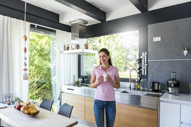 Laughing woman at home in kitchen with cup of coffee - DIGF04447