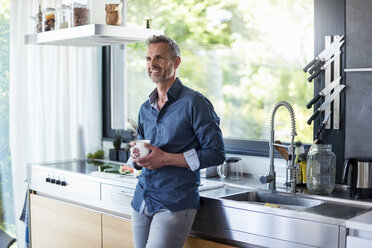 Lächelnder reifer Mann zu Hause in der Küche mit einer Tasse Kaffee - DIGF04449