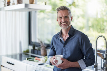 Porträt eines lächelnden reifen Mannes zu Hause in der Küche mit einer Tasse Kaffee - DIGF04450