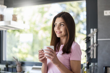 Smiling woman at home in kitchen with cup of coffee - DIGF04452