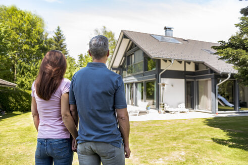 Ehepaar steht Hand in Hand im Garten ihres Hauses - DIGF04460