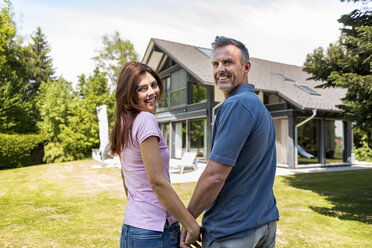 Smiling couple standing hand in hand in garden of their home - DIGF04461