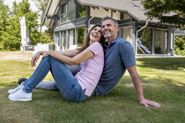 Happy couple sitting in garden of their home - DIGF04466