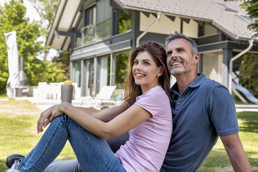 Happy couple sitting in garden of their home - DIGF04467