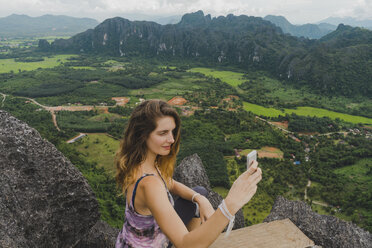 Laos, Vang Vieng, junge Frau auf einem Felsen, die ein Selfie macht - AFVF00519