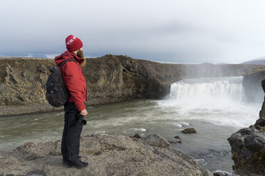 Island, Nordisland, junger Mann schaut zum Wasserfall - AFVF00530