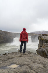 Island, Nordisland, junger Mann schaut zum Wasserfall - AFVF00533