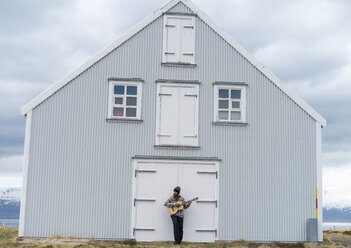Island, junger Mann spielt Gitarre, Holzhaus - AFVF00538