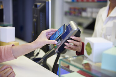 Customer paying cashless with smartphone in a pharmacy - ABIF00400