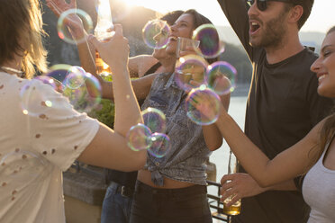 Erwachsene Freunde spielen mit schwimmenden Seifenblasen auf einer Dachterrassenparty - ISF02199