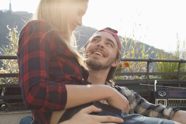 Young woman sitting on boyfriend's lap on roof terrace - ISF02220