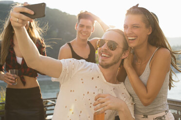 Young man taking selfie with female friend at waterfront roof terrace party, Budapest, Hungary - ISF02235