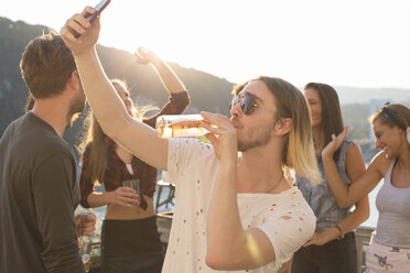 Junger Mann macht ein Selfie beim Biertrinken auf einer Dachterrassenparty am Wasser, Budapest, Ungarn - ISF02236