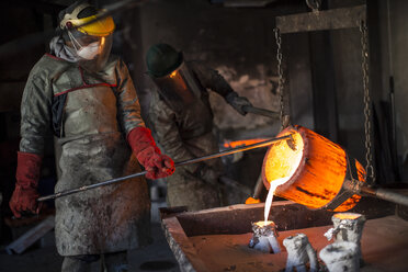 Metallarbeiter in der Gießerei, die geschmolzene Bronze gießen - ISF02260
