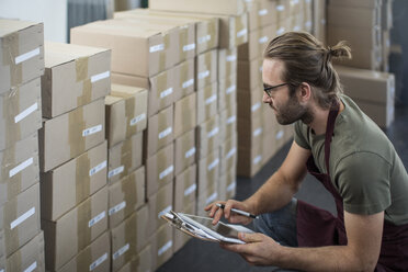 Mann mit digitalem Tablet zur Kontrolle verpackter Produkte im Lagerraum einer Fabrik - ISF02315