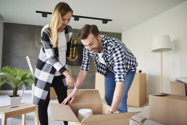 Happy couple moving into new flat unpacking cardboard box - ABIF00418