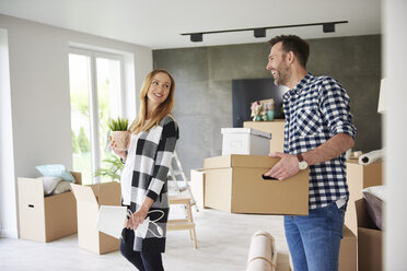 Happy couple moving house carrying cardboard box and plant - ABIF00419