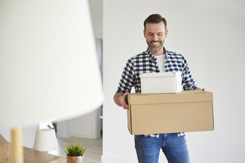 Glücklicher Mann zieht in eine neue Wohnung und trägt einen Karton, lizenzfreies Stockfoto