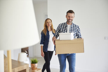 Glückliches Paar zieht in eine neue Wohnung ein und trägt einen Karton - ABIF00421