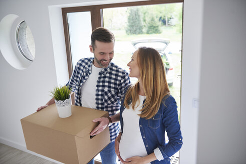Glücklicher Mann und schwangere Frau ziehen in eine neue Wohnung und tragen einen Karton - ABIF00424