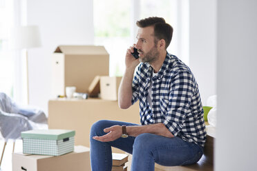 Seriöser Mann, der in eine neue Wohnung einzieht und mit seinem Handy telefoniert - ABIF00428