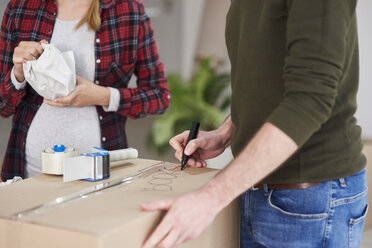 Couple moving house packing and labelling cardboard boxes - ABIF00447