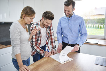 Couple with real estate agent signing contract in kitchen of new apartment - ABIF00450