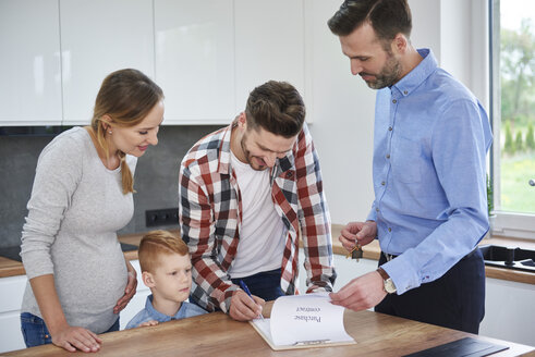 Familie mit Immobilienmakler bei der Vertragsunterzeichnung in der Küche der neuen Wohnung - ABIF00453