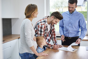 Family with real estate agent signing contract in kitchen of new apartment - ABIF00454