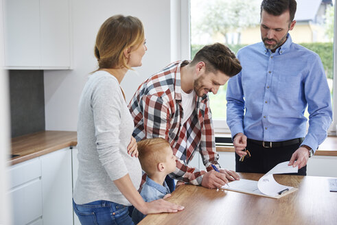 Familie mit Immobilienmakler bei der Vertragsunterzeichnung in der Küche der neuen Wohnung - ABIF00454