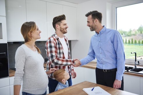 Familie und Immobilienmakler schütteln sich in der Küche der neuen Wohnung die Hände - ABIF00455