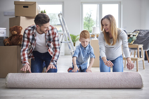 Familie rollt einen Teppich in der neuen Wohnung aus, lizenzfreies Stockfoto