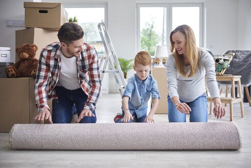 Familie rollt einen Teppich in der neuen Wohnung aus - ABIF00462
