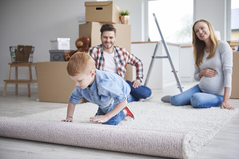 Junge mit Eltern beim Ausrollen eines Teppichs in der neuen Wohnung, lizenzfreies Stockfoto