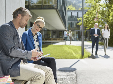 Colleagues with tablet sitting on bench outside office building - CVF00589