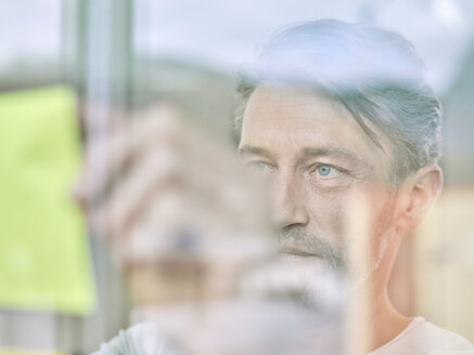 Businessman looking at sticky note at glass pane - CVF00606