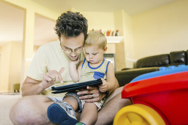 Vater und kleiner Sohn spielen zusammen zu Hause und schauen auf ein digitales Tablet - ISF02368